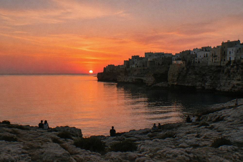 Cliff-top town in silhouette against a pink and orange sunset over a calm sea