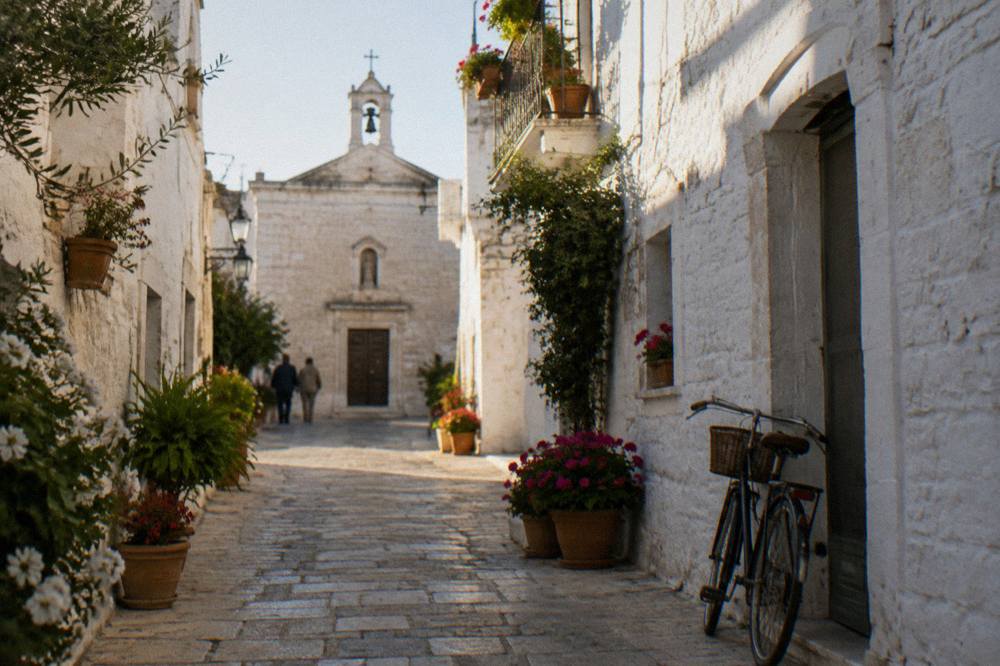 White lane with flower pots, a tiny church front and a bicycle leaning on the wall