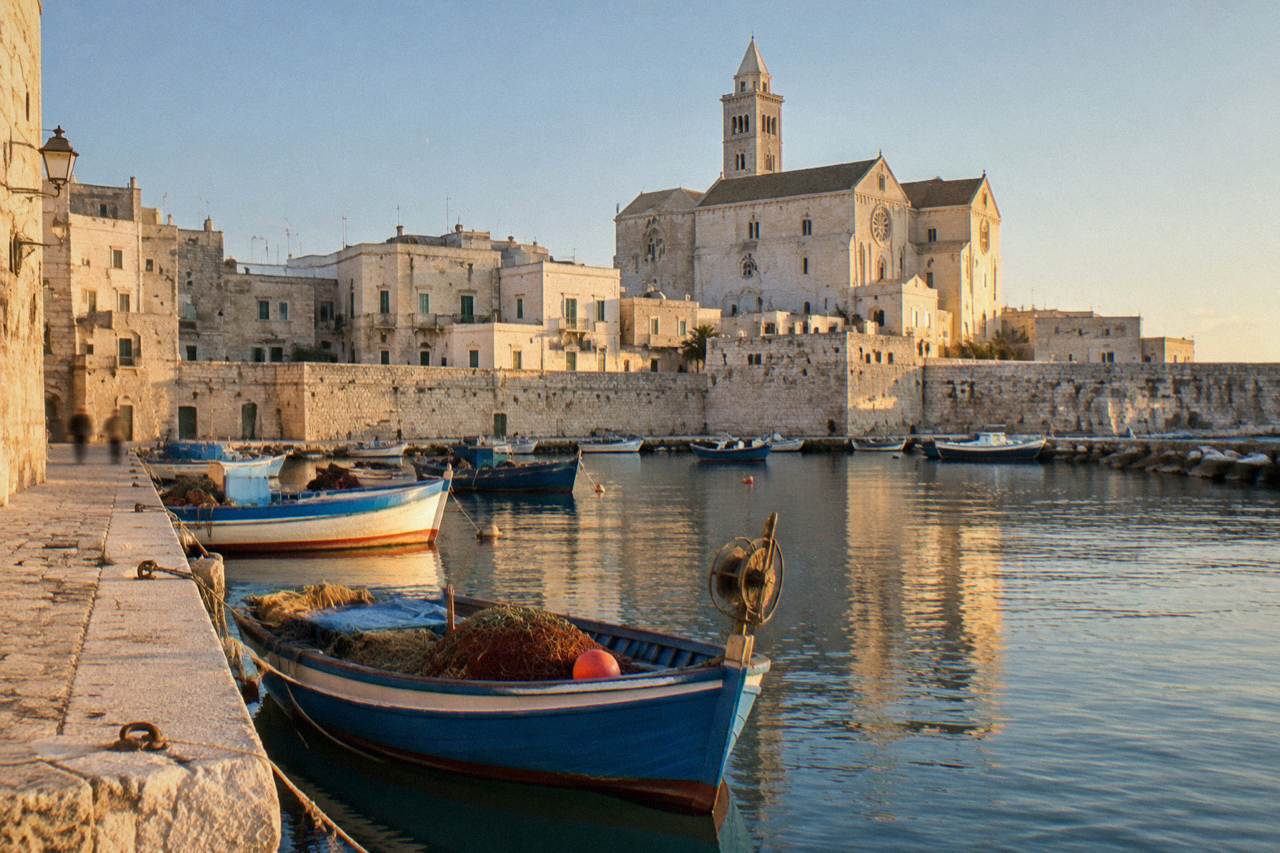 Small harbour town with old fishing boats in a stone-walled inlet and a pale stone cathedral behind