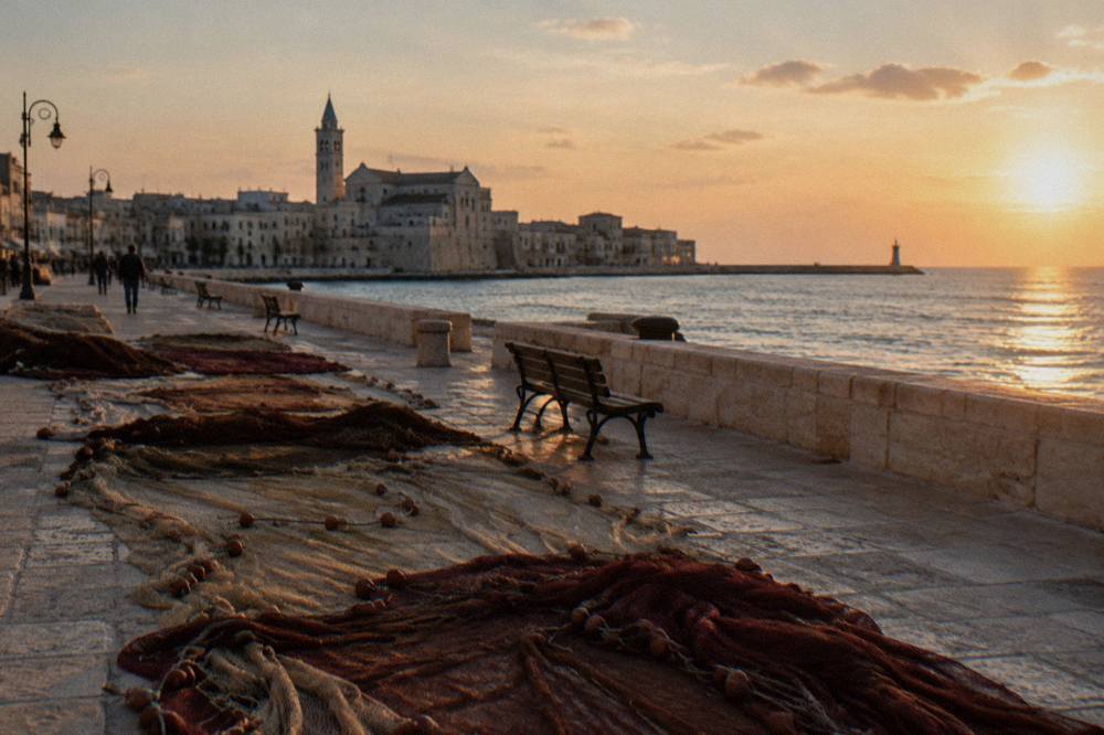Long seafront with a low wall, benches and fishing nets laid out to dry on the stones