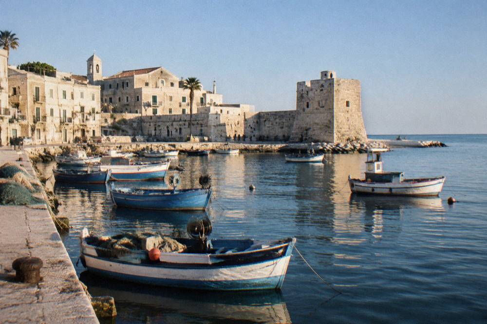 Small harbour of fishing boats under the pale walls of an old town with a squat stone tower