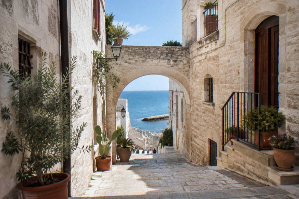 Pale old town lane with an arch and stone steps leading towards the sea with potted plants