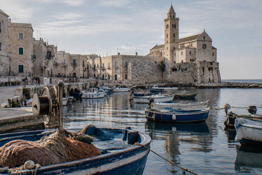 Small harbour town with old fishing boats in a stone-walled inlet and a pale stone cathedral behind