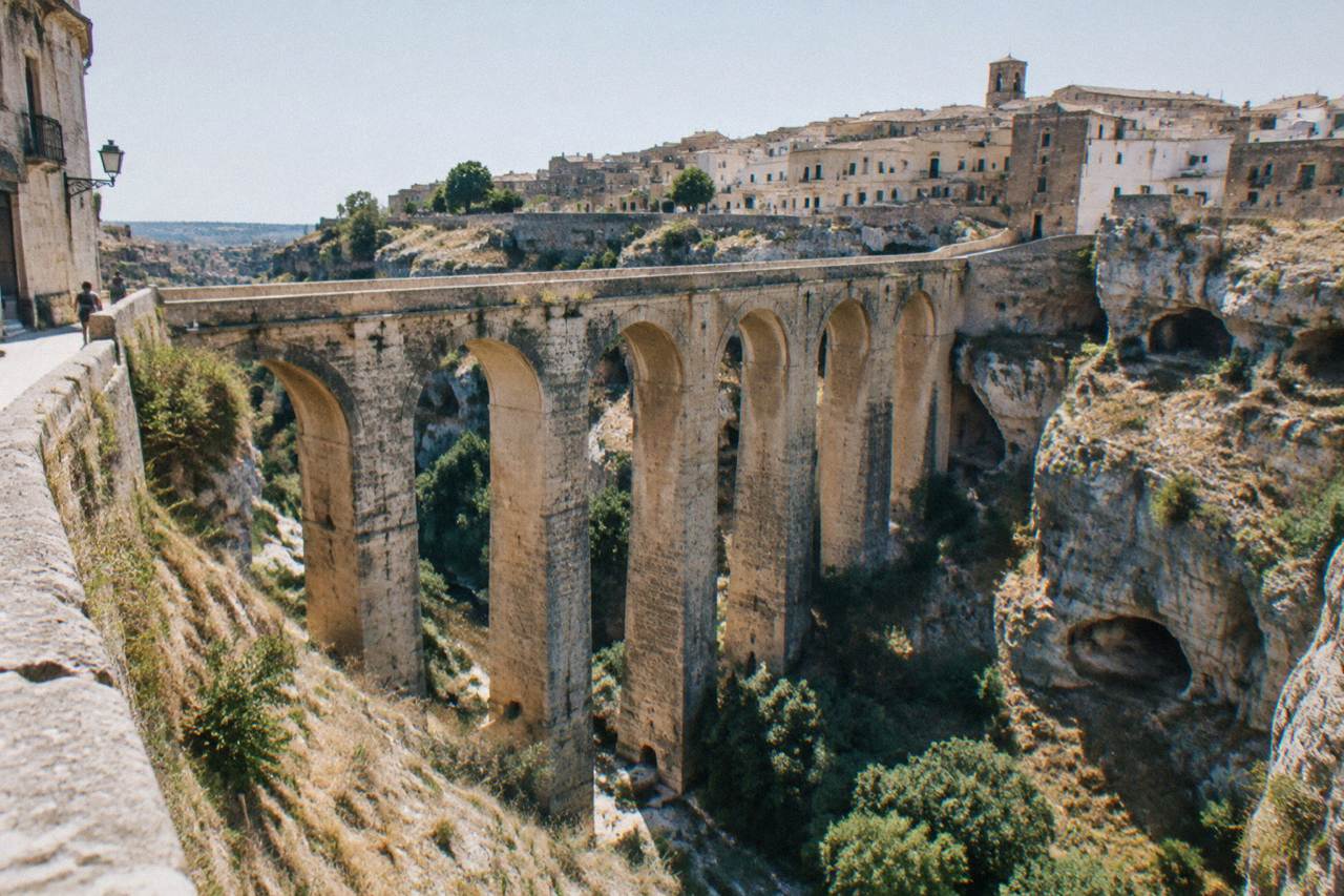 Deep rocky ravine crossed by a tall many-arched stone bridge with old town houses on the far rim