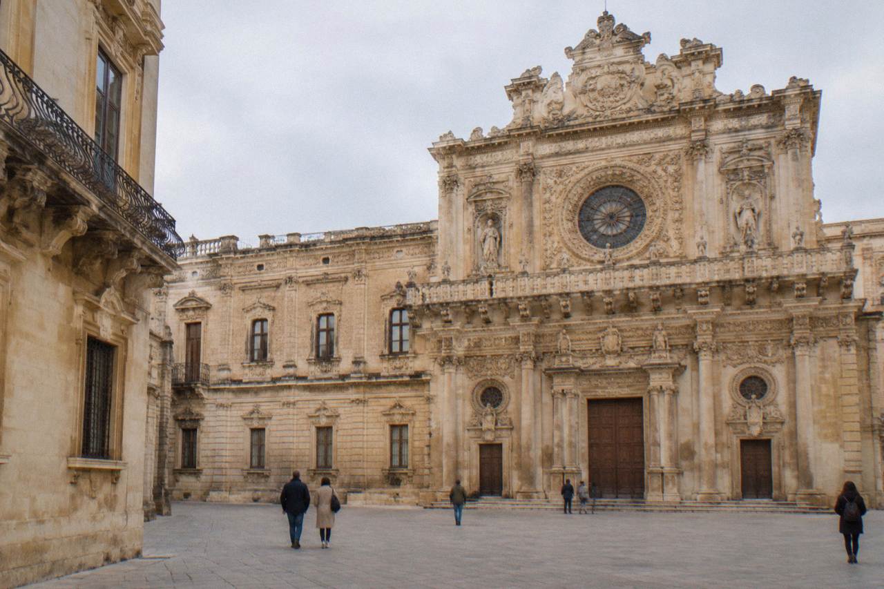 Richly carved baroque church facade of honey-coloured limestone with ornate balconies and a rose window