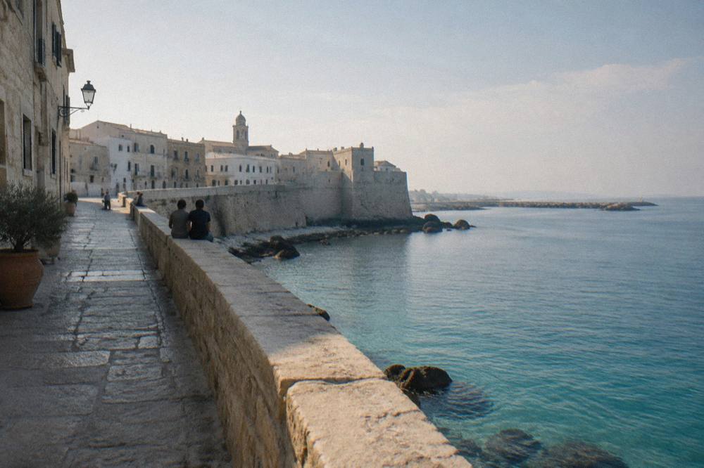 Sea promenade along an old town wall above calm turquoise water with distant people sitting on the wall