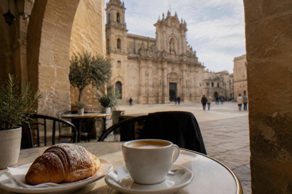 Cafe terrace under a stone arch with a cup of coffee and a pastry on a small table