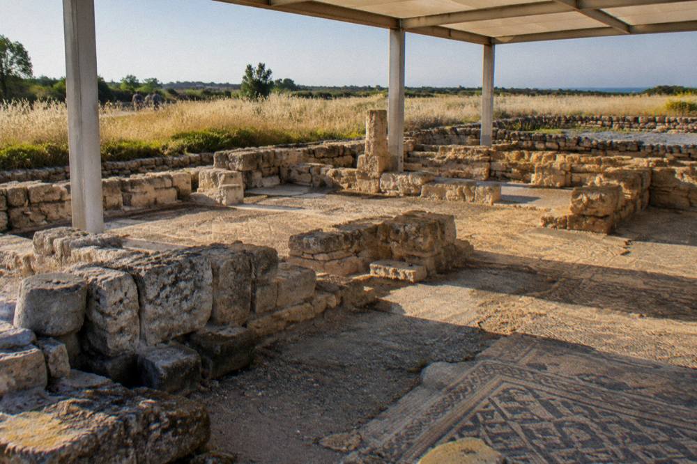 Stone foundations of an ancient basilica with patches of mosaic floor under a light shelter