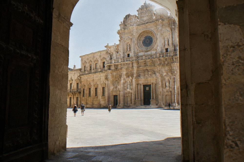Richly carved baroque church facade of honey-coloured limestone with ornate balconies and a rose window