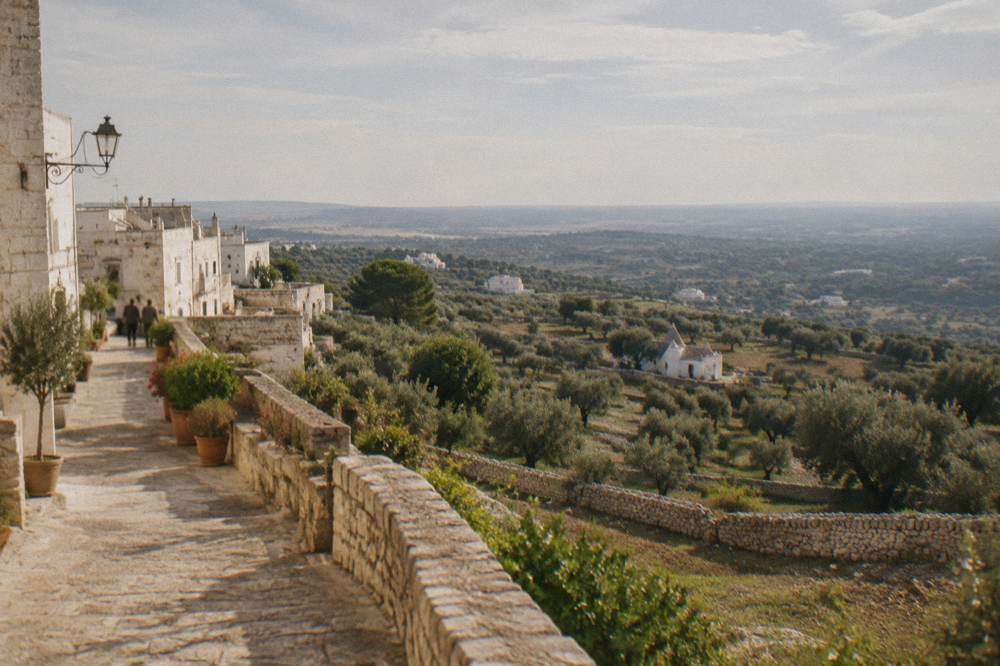 View from a hill town over olive groves and low dry-stone walls to a hazy plain