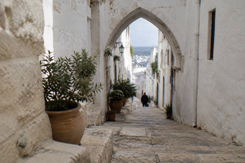 Steep whitewashed alley with stone steps, a pointed arch overhead and potted plants