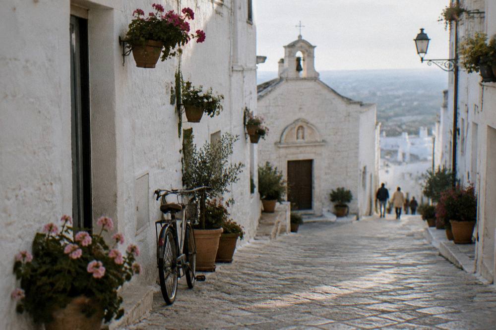 White lane with flower pots, a tiny church front and a bicycle leaning on the wall