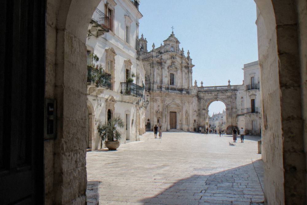 Baroque town square with cream and white facades, wrought-iron balconies and an arched gateway