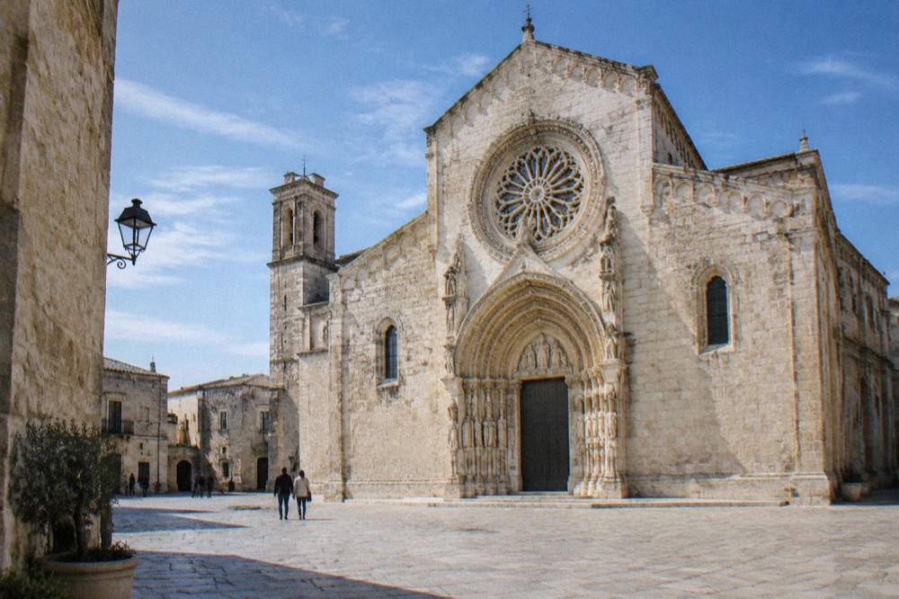 Romanesque cathedral in warm limestone with a carved rose window and portal on a small square