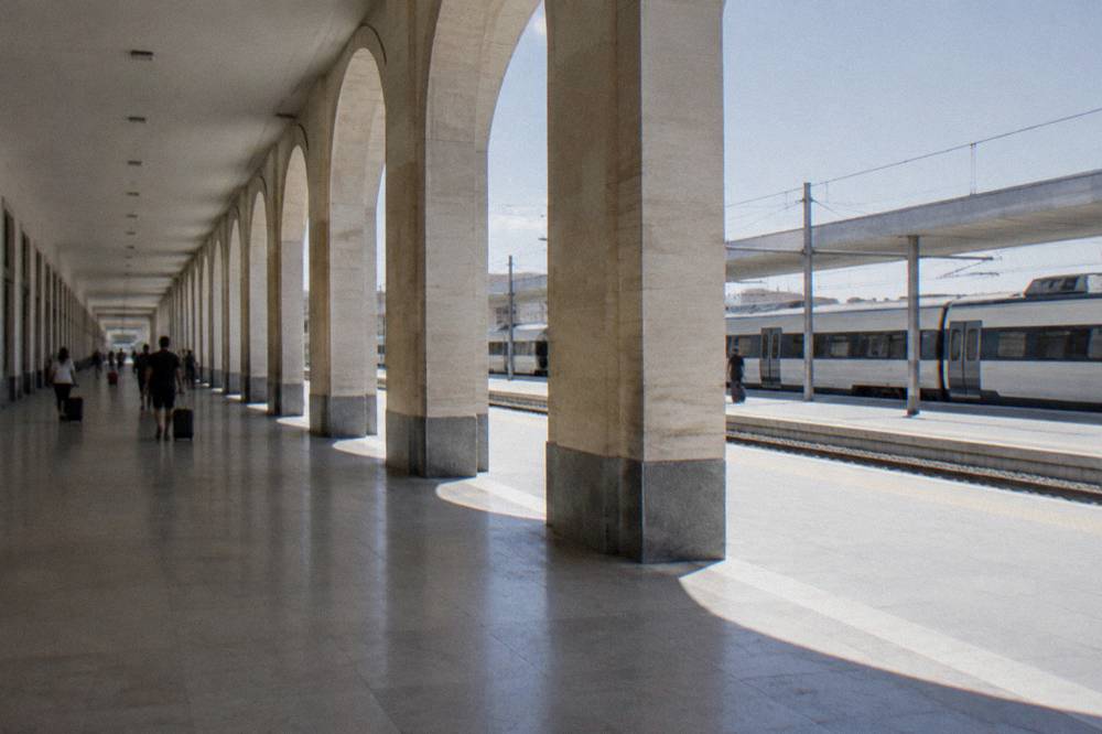 Large pale railway station with a long concourse, distant travellers with suitcases and plain trains at the platforms