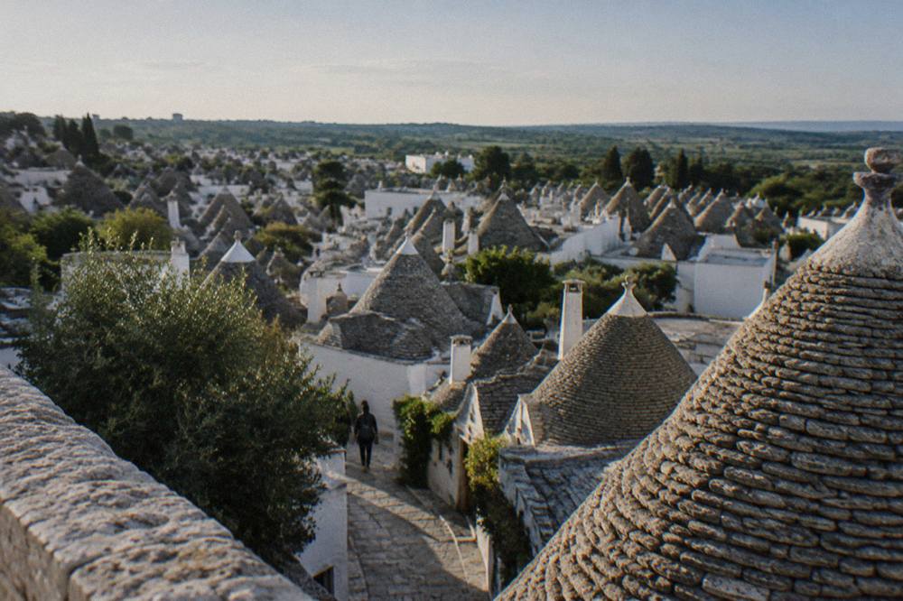 Wide view over a dense cluster of grey conical stone roofs from a raised belvedere