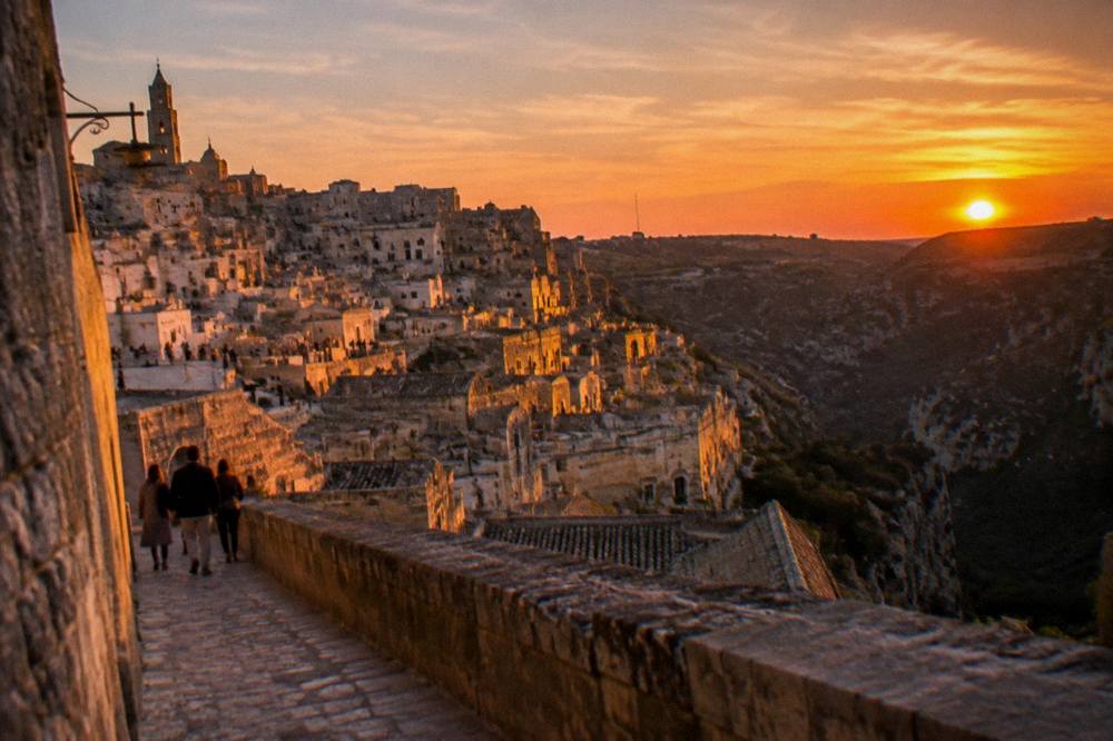 Sunset gold on stacked rooftops and cave facades of an ancient stone town above a shadowed ravine