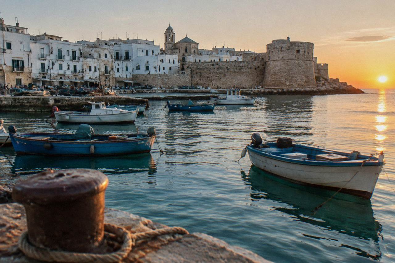 Old harbour of small painted wooden boats with a stone castle on the headland and a whitewashed old town behind
