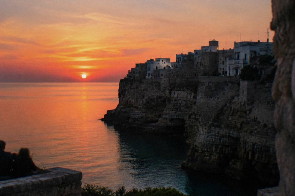 Cliff-top town in silhouette against a pink and orange sunset over a calm sea