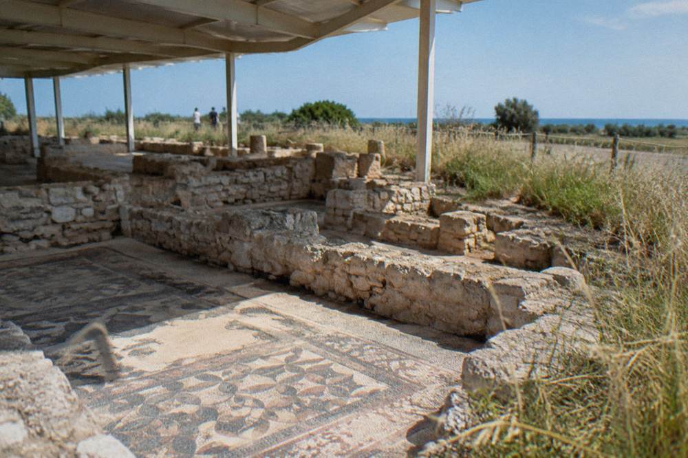 Stone foundations of an ancient basilica with patches of mosaic floor under a light shelter