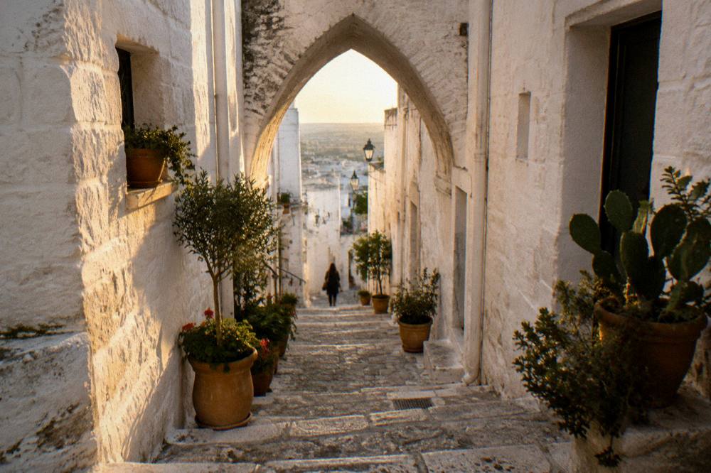 Steep whitewashed alley with stone steps, a pointed arch overhead and potted plants