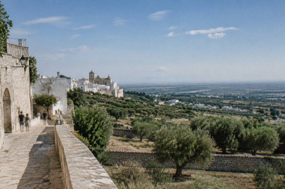 View from a hill town over olive groves and low dry-stone walls to a hazy plain