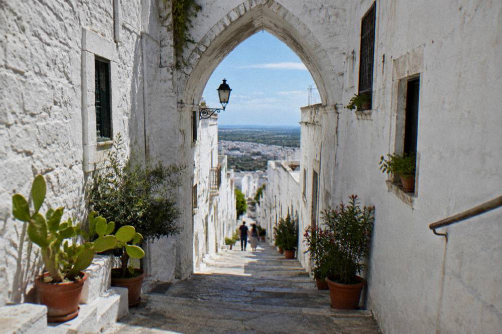 Steep whitewashed alley with stone steps, a pointed arch overhead and potted plants