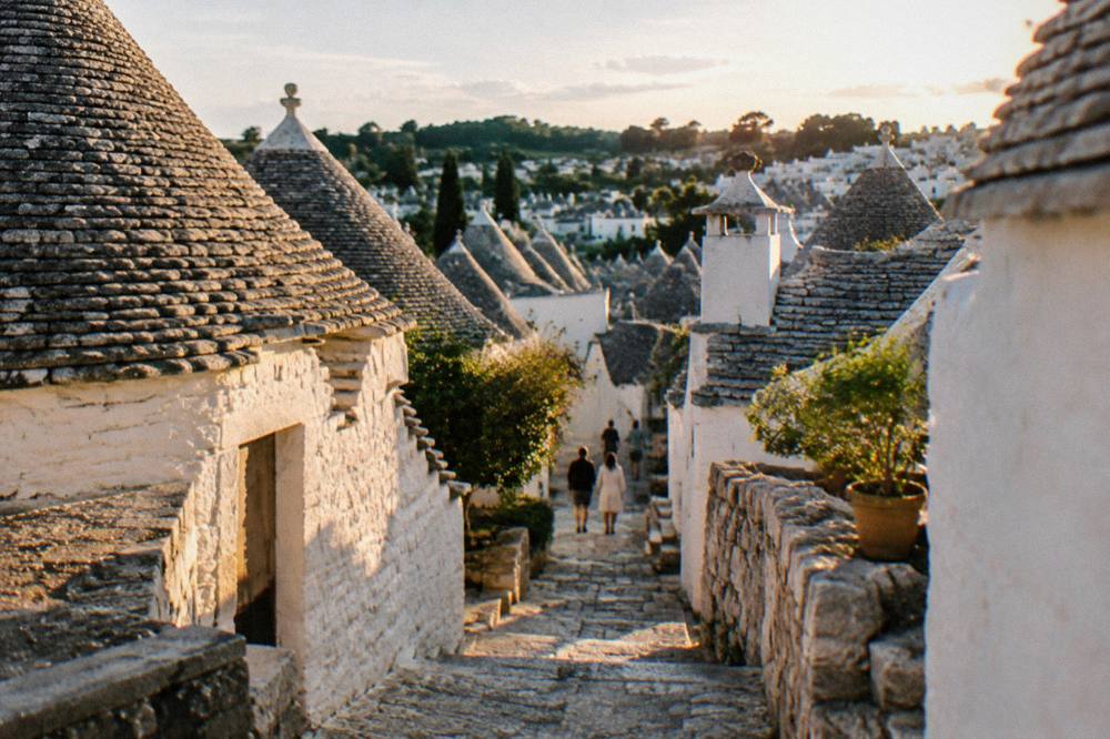 Hillside of white dry-stone houses with grey conical stone roofs and a narrow stepped lane between them