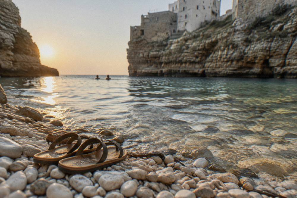 White pebbles and clear shallow water at the edge of a cove with a pair of sandals left on the stones