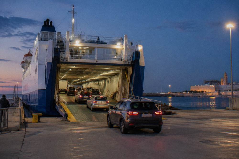 Ferry vehicle deck seen from the quay with rows of cars driving in under floodlights at evening
