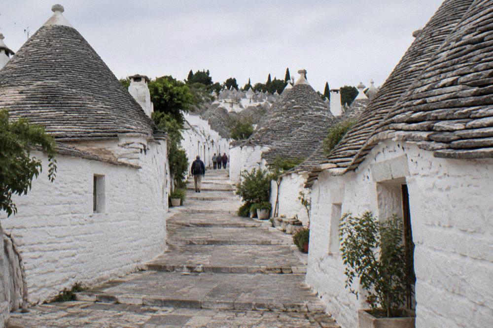 Hillside of white dry-stone houses with grey conical stone roofs and a narrow stepped lane between them
