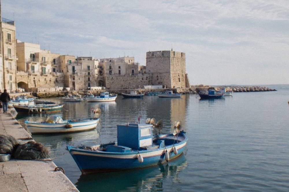 Small harbour of fishing boats under the pale walls of an old town with a squat stone tower