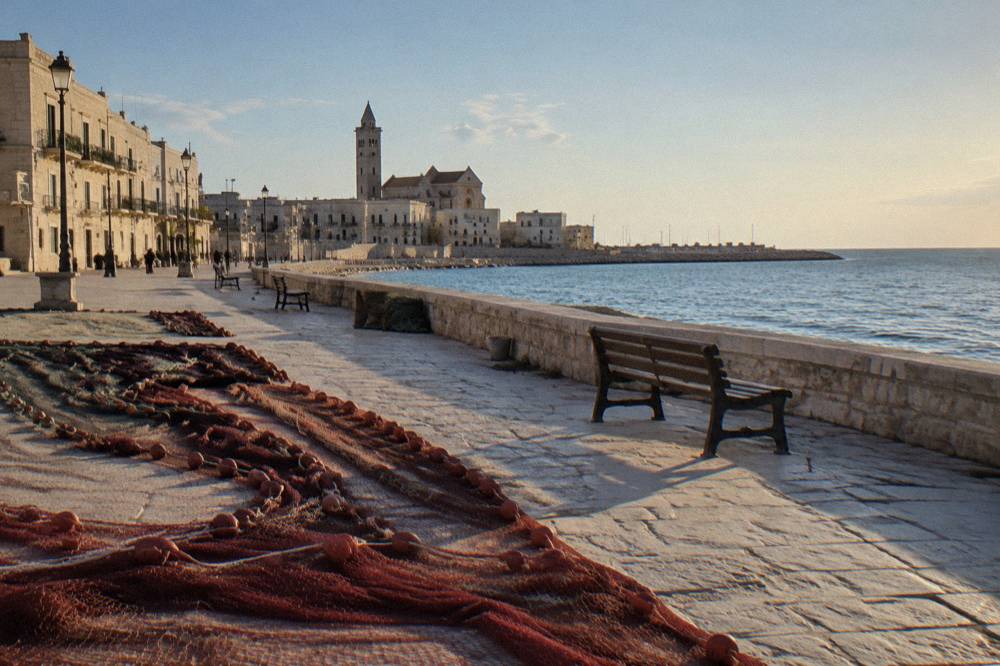 Long seafront with a low wall, benches and fishing nets laid out to dry on the stones