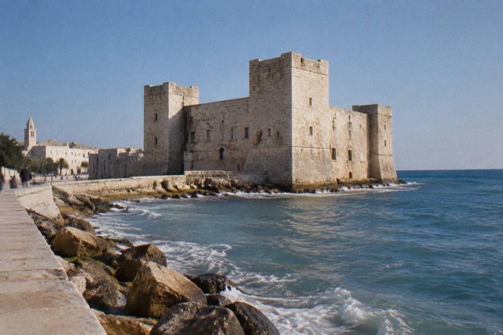 Square stone castle with corner towers on a low shore with waves lapping its base
