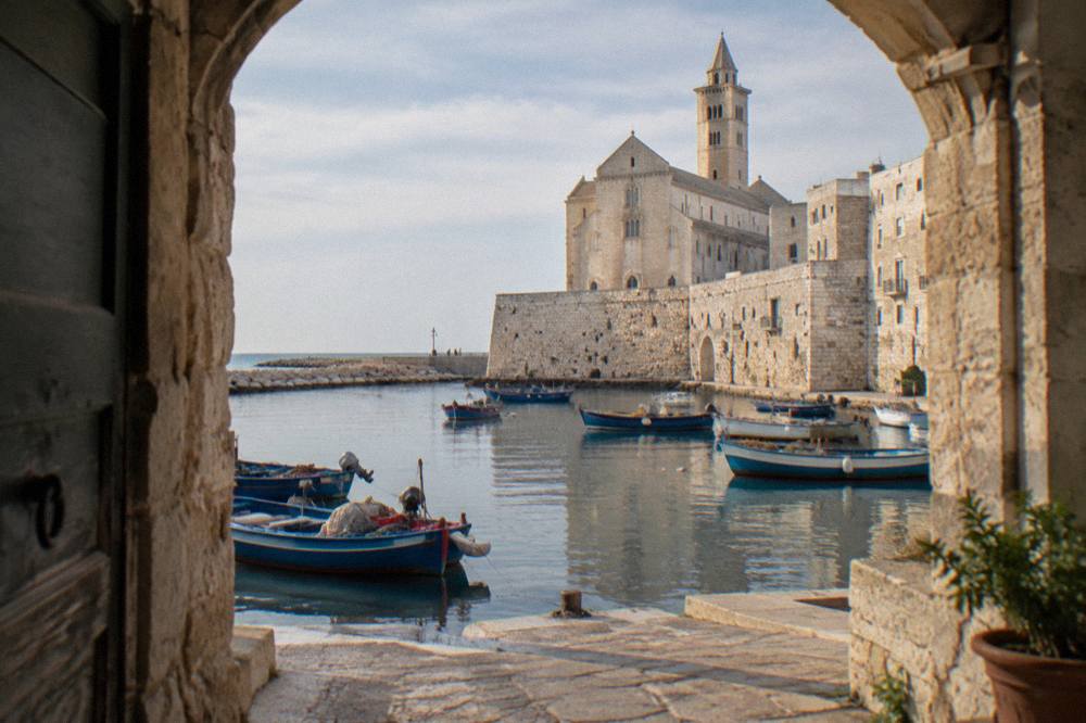 Small harbour town with old fishing boats in a stone-walled inlet and a pale stone cathedral behind