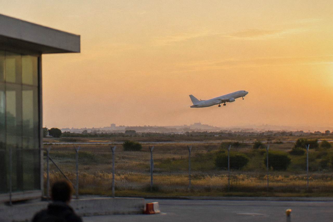 Plane taking off low over scrubby fields beyond a perimeter fence at golden hour