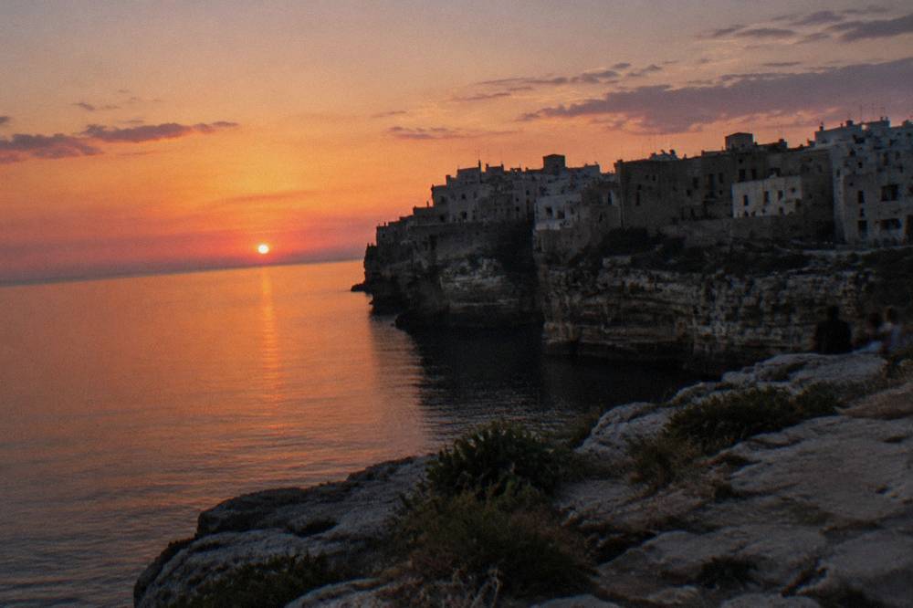 Cliff-top town in silhouette against a pink and orange sunset over a calm sea
