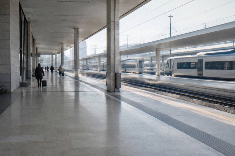 Large pale railway station with a long concourse, distant travellers with suitcases and plain trains at the platforms