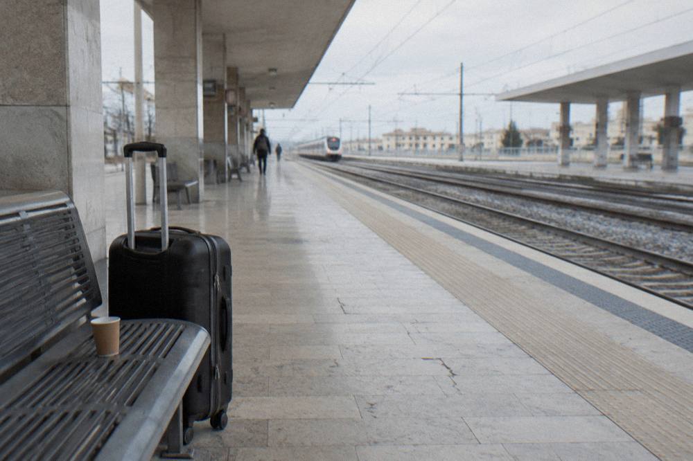 Platform bench with a suitcase and a paper cup beside empty tracks and a distant plain train