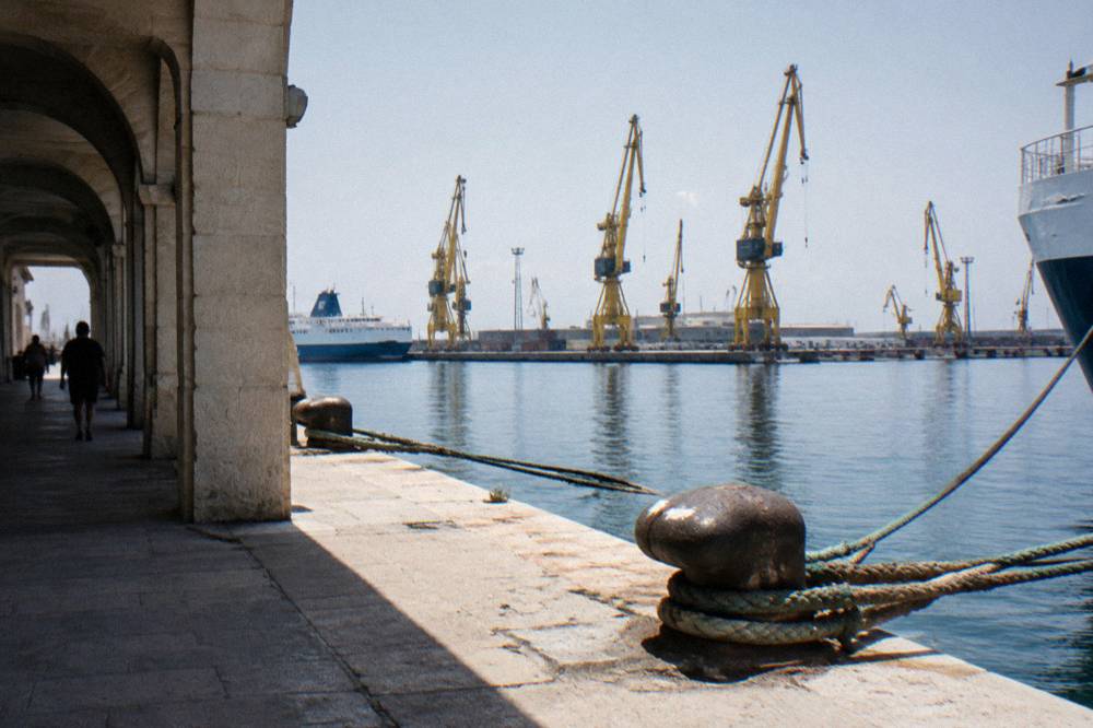 Row of harbour cranes behind a calm commercial dock with ropes and bollards in the foreground