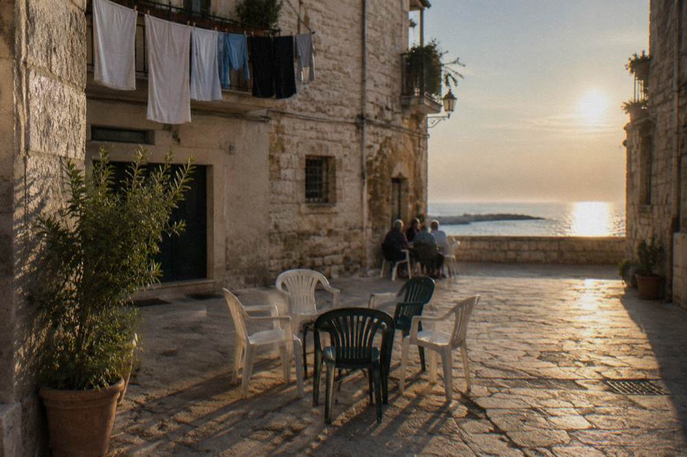 Tiny square where plastic chairs are drawn up in a circle and elderly residents chat far off in the shade