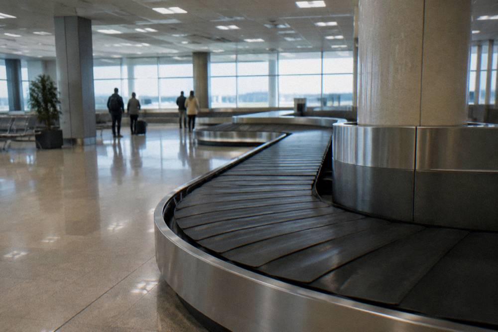 Baggage reclaim hall with an empty belt curving through and a few travellers watching far off