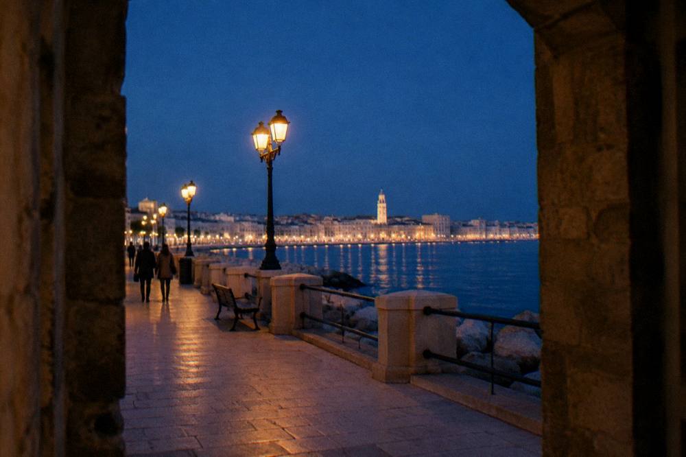 Seafront promenade at blue hour with lit street lamps and the lights of the old town across the bay