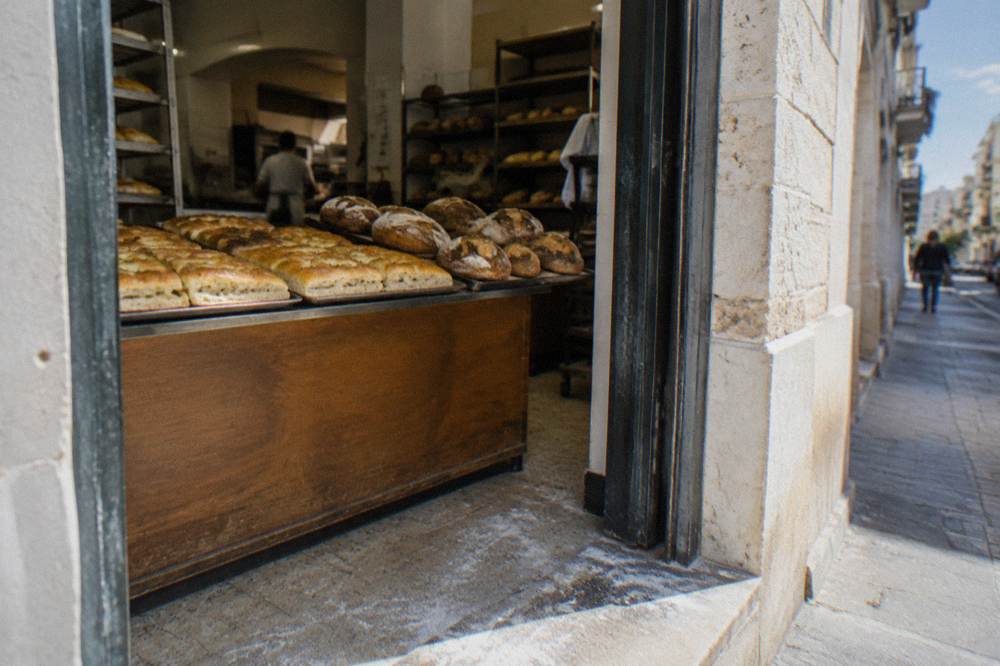 Neighbourhood bakery doorway with trays of golden focaccia and round loaves seen from the street