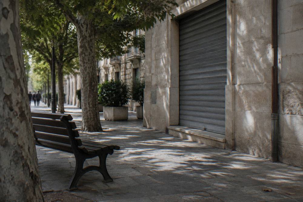 Shaded corner of a district with a cream stone shopfront, a bench and dappled light