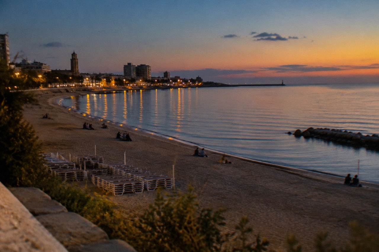City beach in the evening with distant people on the sand, stacked sunbeds and an almost still sea