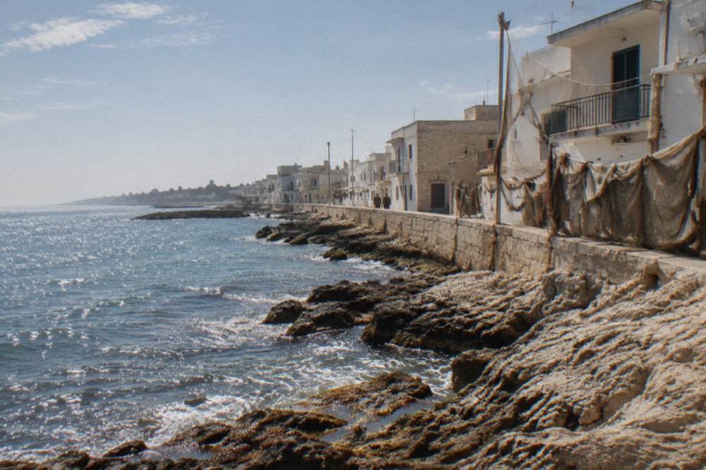 Rocky shore beside simple seafront houses with nets drying in hazy morning light