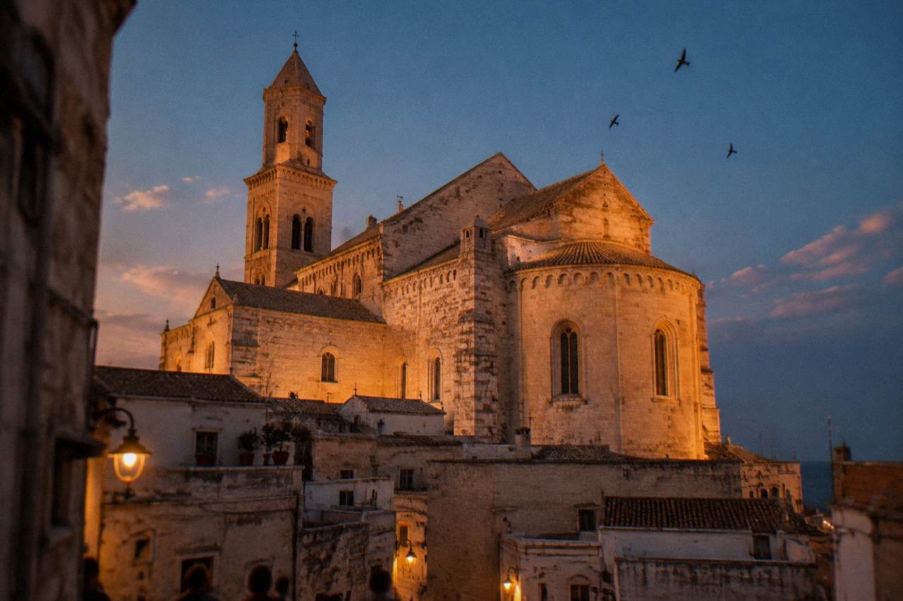 Basilica apse and walls glowing in low evening light above old town rooftops with swifts in the sky