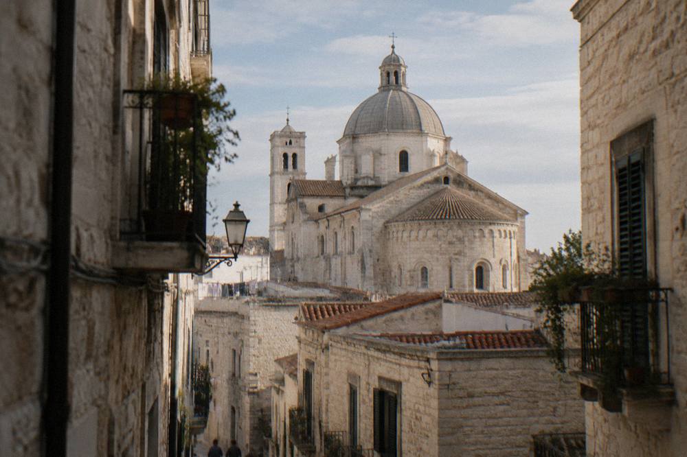 Cathedral dome and apse rising above terracotta rooftops at the end of a narrow old-town lane in afternoon light