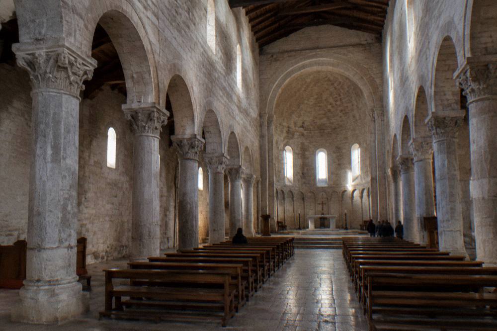 Bare stone cathedral interior with round arches, a high apse and shafts of light from small windows